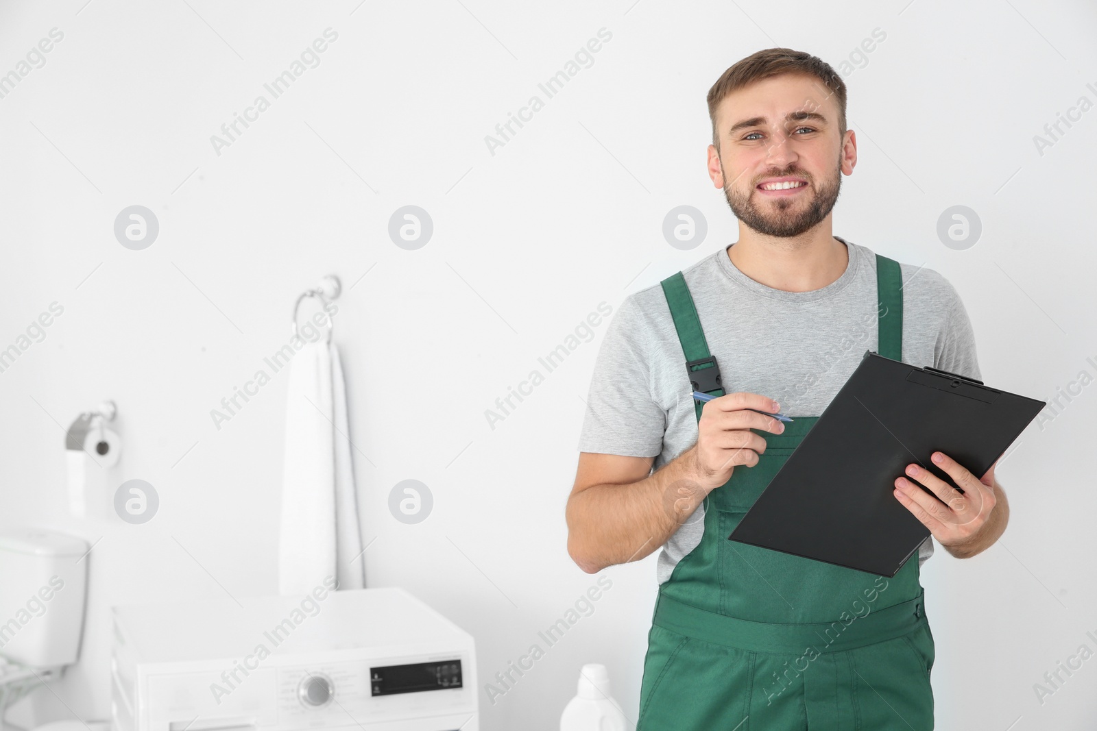 Photo of Young plumber with clipboard near washing machine in bathroom. Space for text