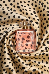 Photo of Luxury perfume in bottle on fabric with leopard pattern, top view