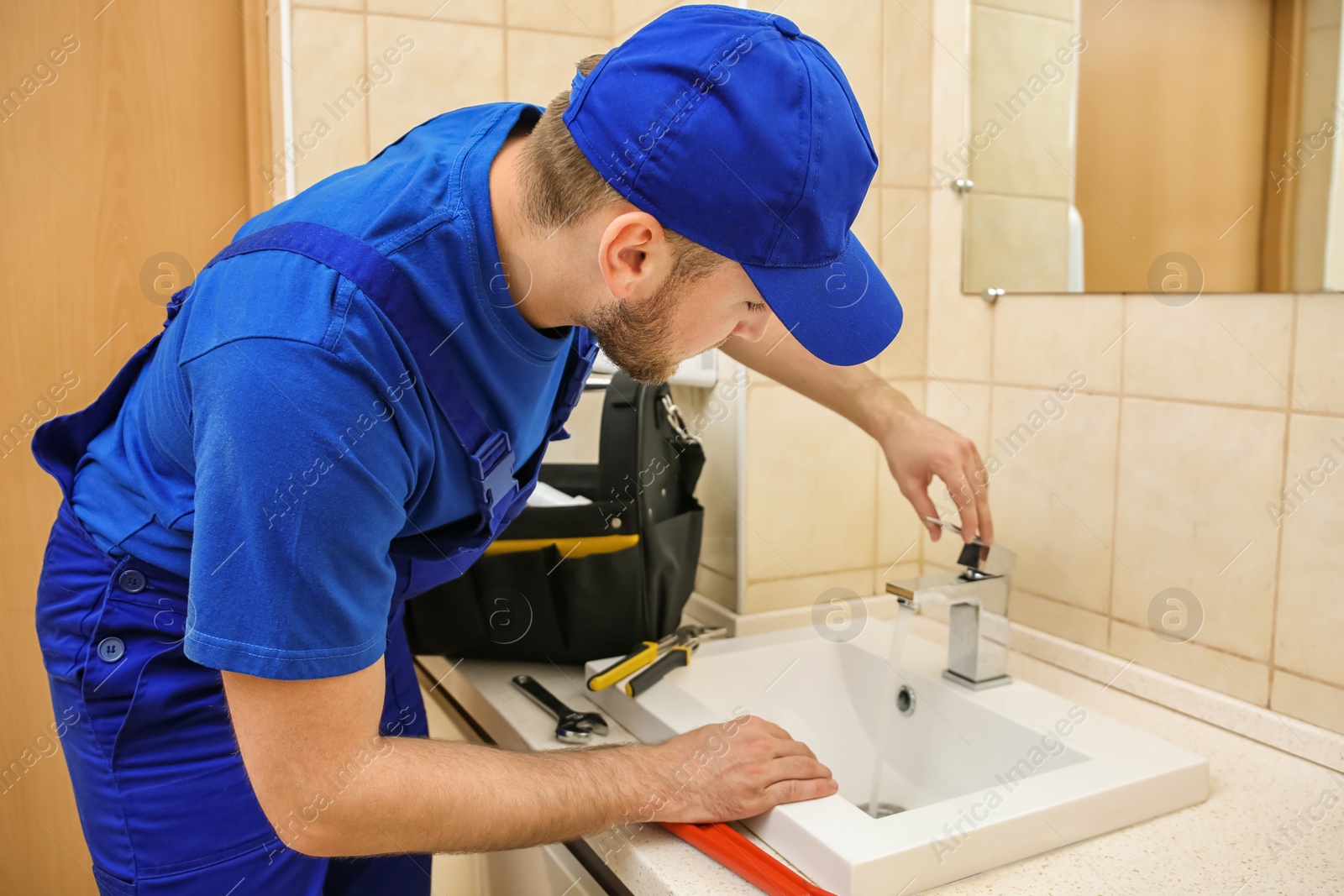 Photo of Professional plumber in uniform fixing sink in bathroom