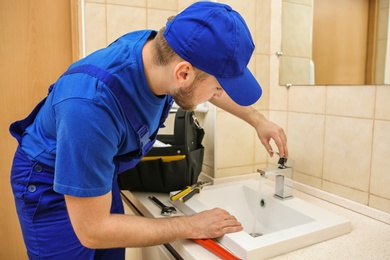 Professional plumber in uniform fixing sink in bathroom