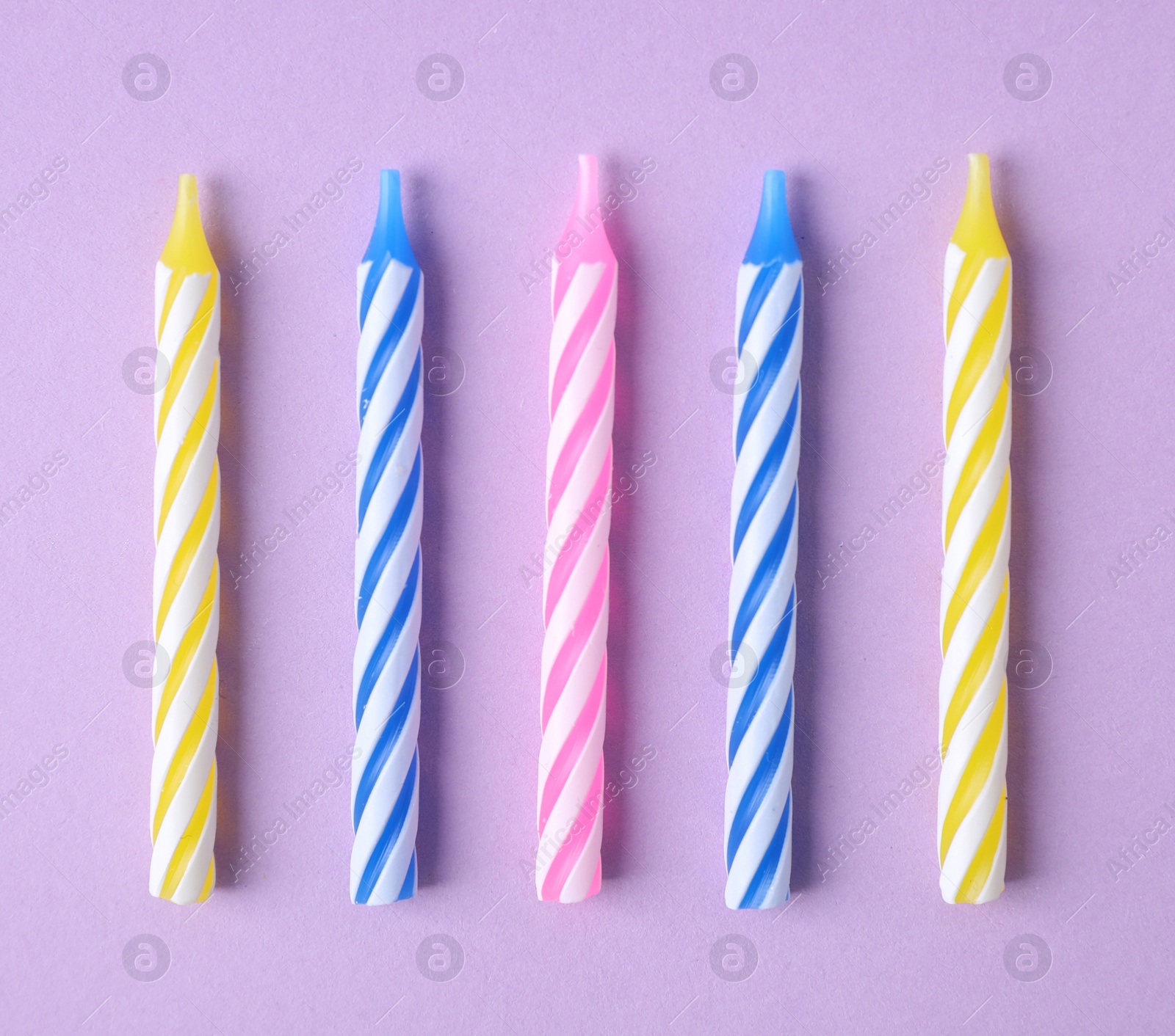 Photo of Colorful striped birthday candles on lilac background, flat lay