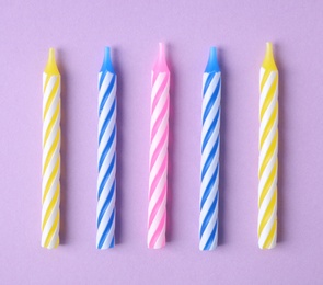 Photo of Colorful striped birthday candles on lilac background, flat lay