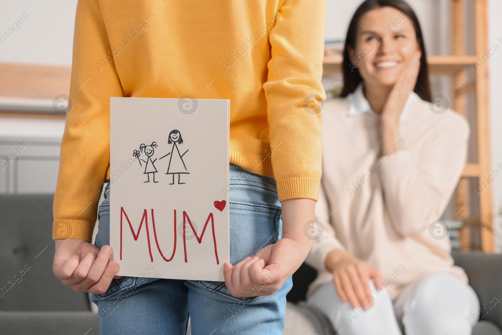 Photo of Little girl hiding greeting card for her mother behind back at home