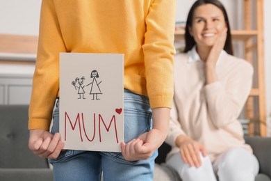 Little girl hiding greeting card for her mother behind back at home