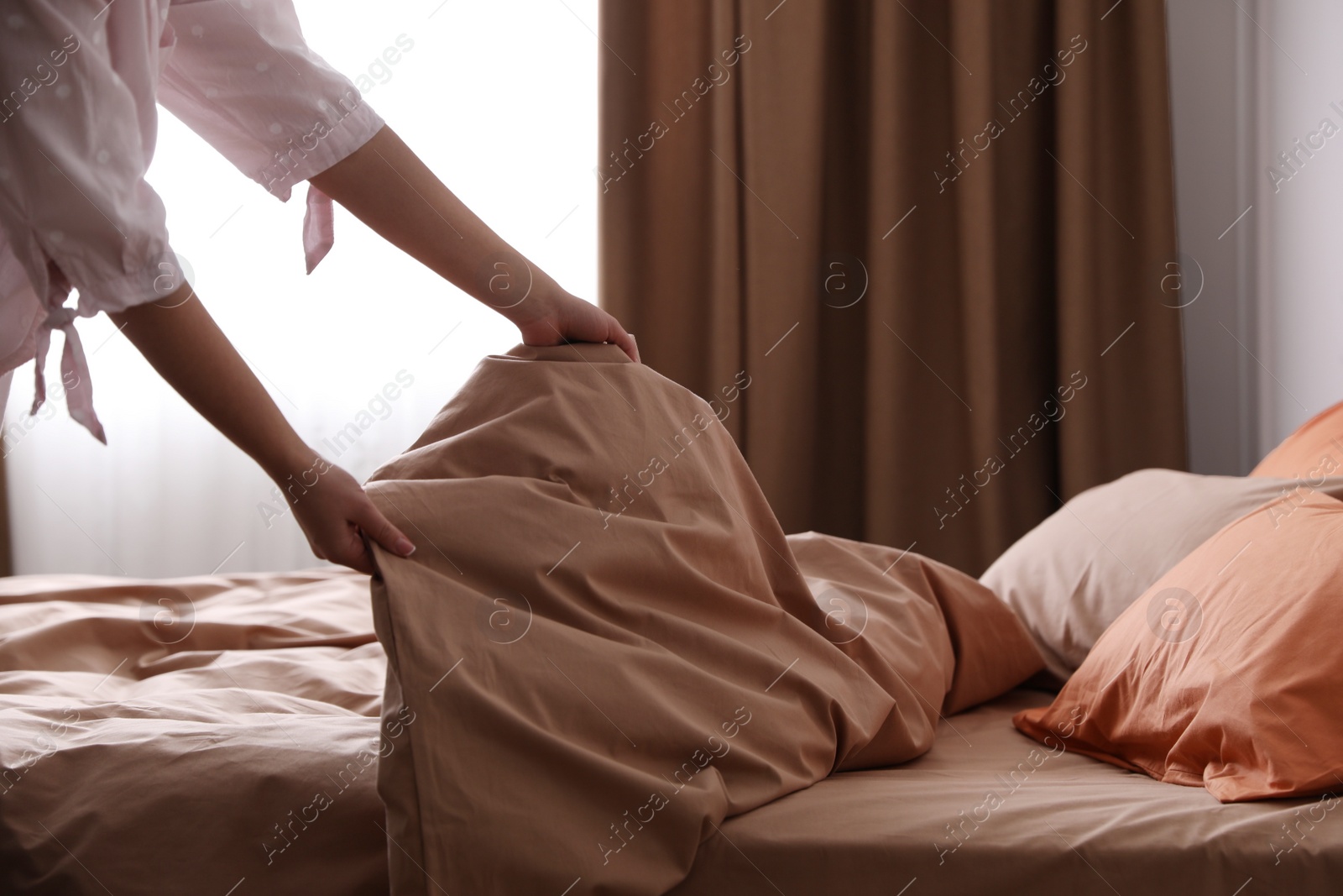 Photo of Woman making bed with brown linens and orange pillows, closeup