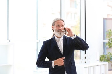 Photo of Portrait of handsome mature man with mobile phone in suit, indoors