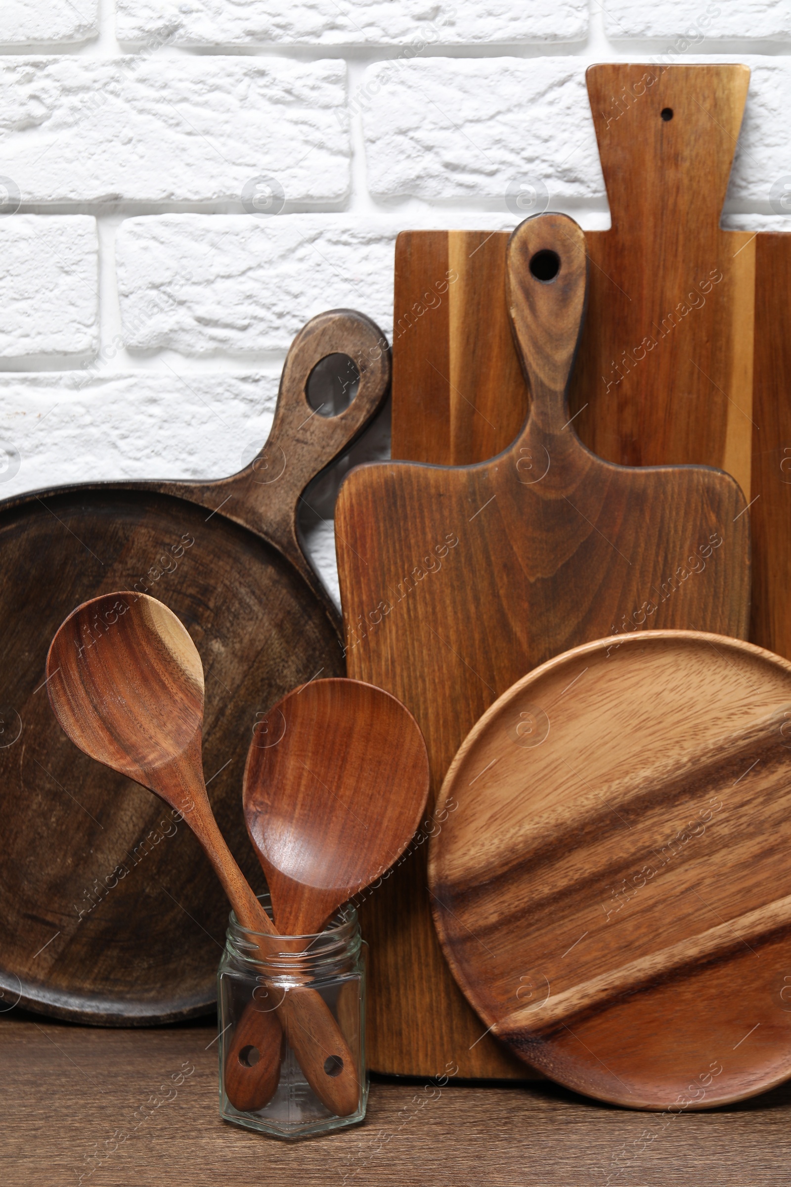 Photo of Different cutting boards and kitchen utensils on wooden table near brick wall