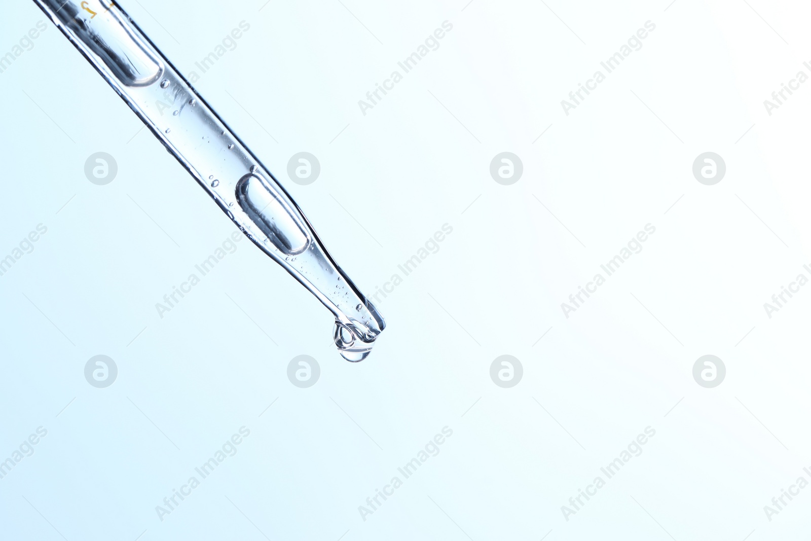 Photo of Dripping liquid from pipette on light blue background, closeup. Space for text