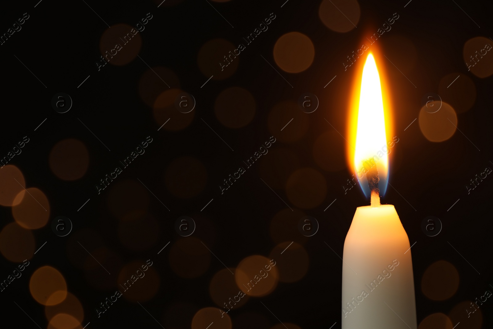 Photo of Burning candle on black background with blurred lights, space for text