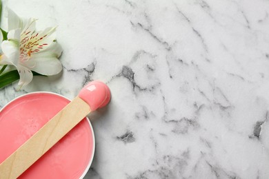 Spatula with wax and flower on white marble table, flat lay. Space for text