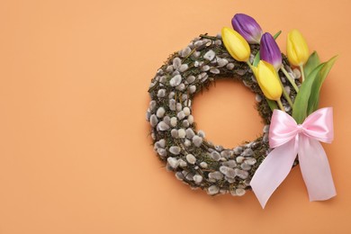Photo of Wreath made of beautiful willow, colorful tulip flowers and pink bow on orange background, top view. Space for text