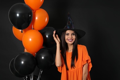 Photo of Beautiful woman wearing witch costume with balloons for Halloween party on black background