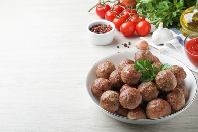 Photo of Tasty cooked meatballs with parsley on white wooden table. Space for text