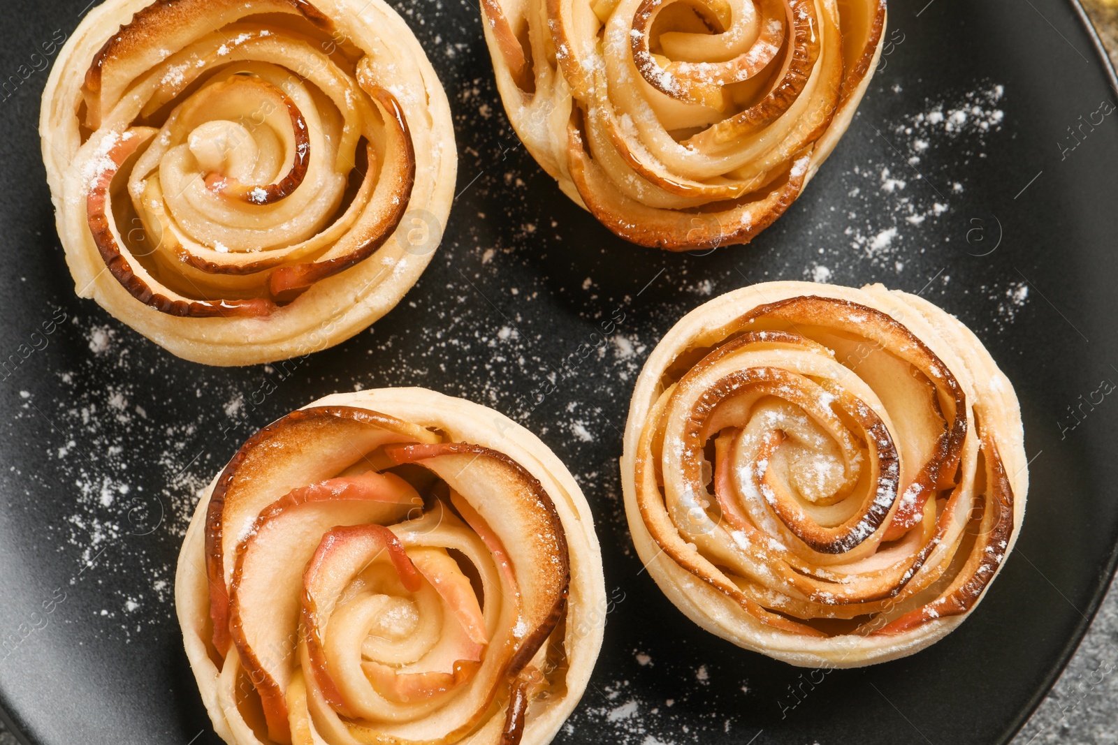 Photo of Freshly baked apple roses on black plate, top view. Beautiful dessert