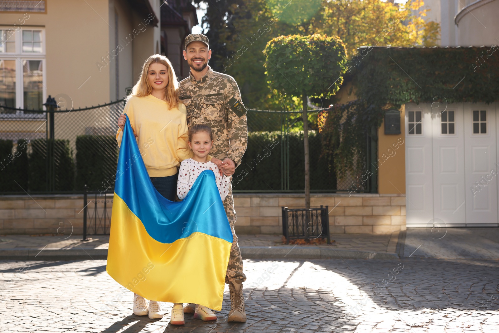 Photo of Soldier in military uniform reunited with his family and Ukrainian flag on city street, space for text