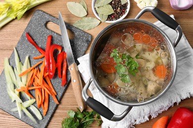 Photo of Pot of delicious vegetable bouillon and ingredients on wooden table, flat lay