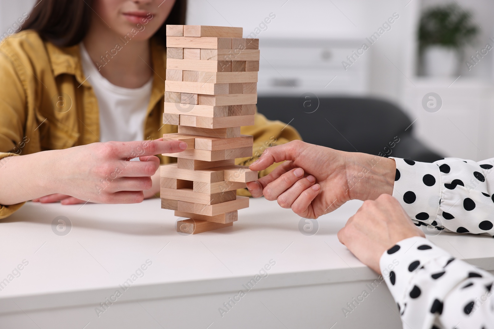 Photo of People playing Jenga tower at white table indoors, closeup