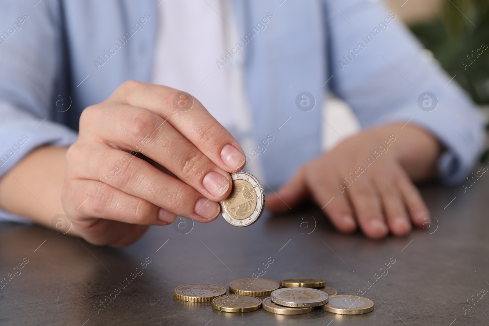 Photo of Poor woman counting coins at grey table indoors, closeup