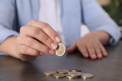 Photo of Poor woman counting coins at grey table indoors, closeup