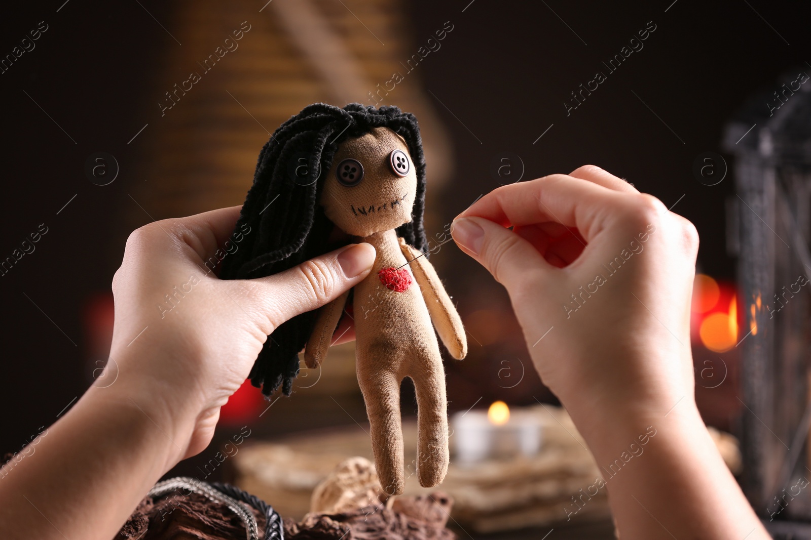 Photo of Woman pricking female voodoo doll's heart with pin at table, closeup