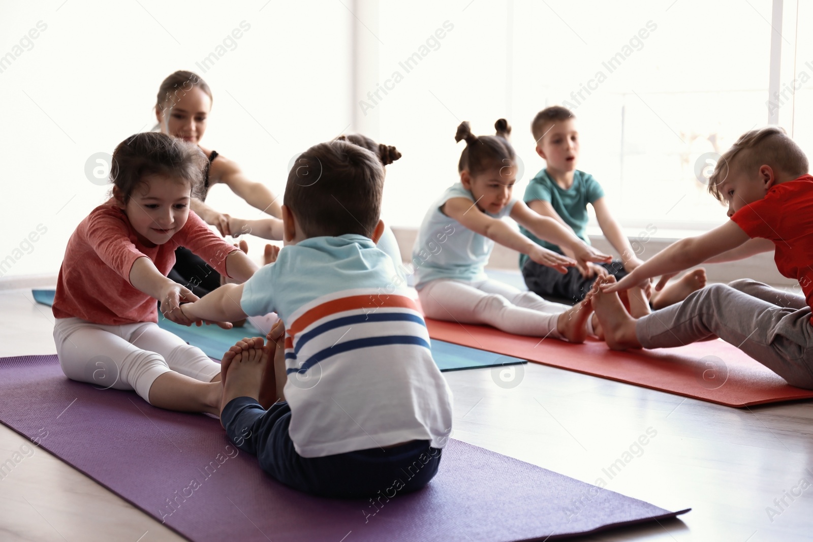 Photo of Little children and their teacher practicing yoga in gym