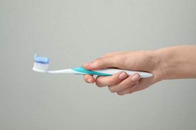 Woman holding toothbrush with paste on light grey background, closeup