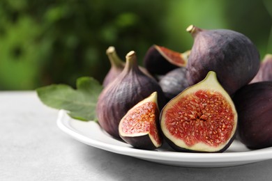 Photo of Whole and cut ripe figs on light table against blurred green background, closeup. Space for text