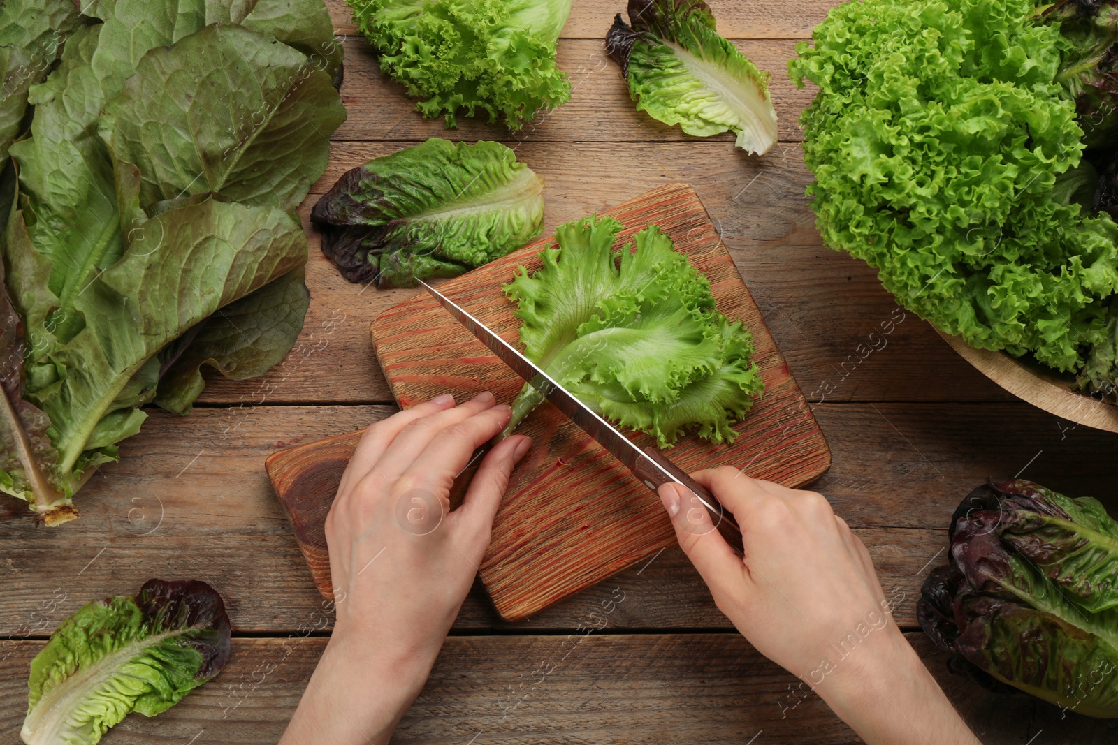 Photo of Woman cutting green lettuce leaf at wooden table, top view