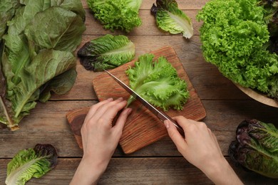 Photo of Woman cutting green lettuce leaf at wooden table, top view