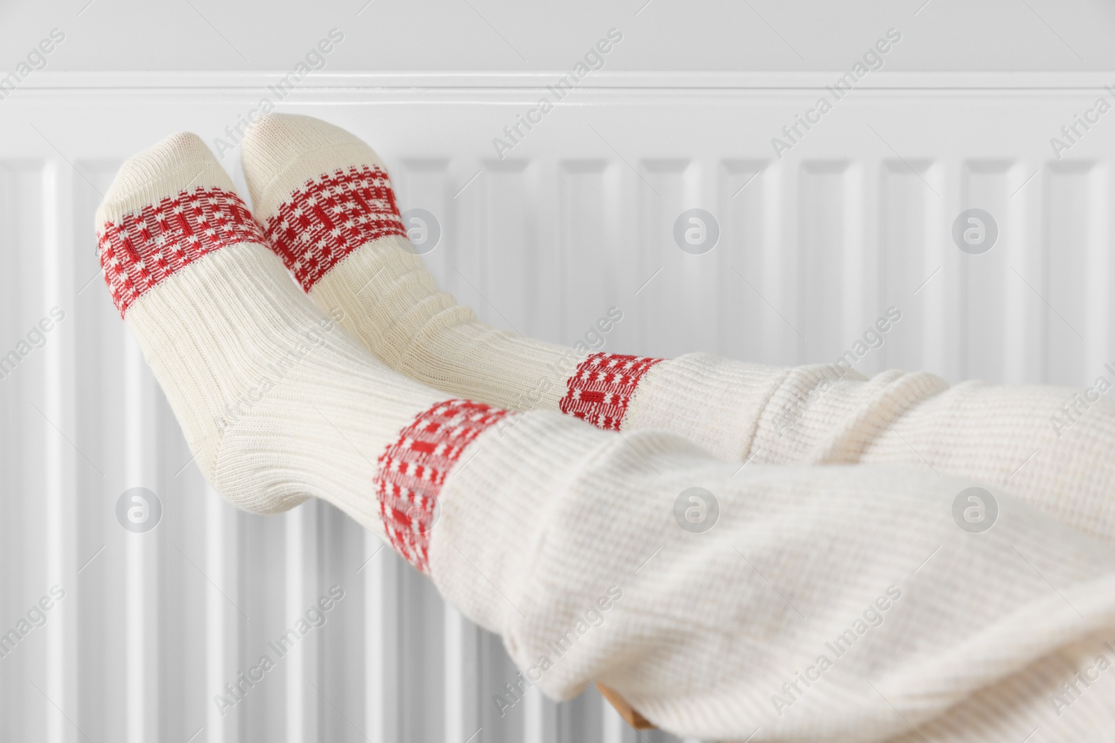 Photo of Little girl warming feet near heating radiator indoors, closeup