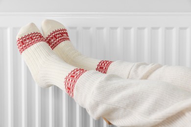 Photo of Little girl warming feet near heating radiator indoors, closeup