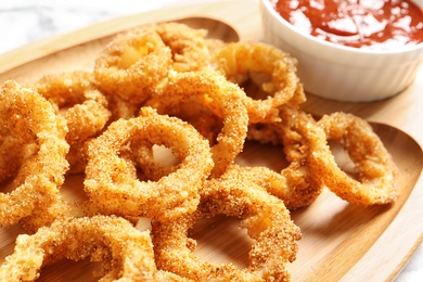 Photo of Homemade crunchy fried onion rings with sauce on wooden dish, closeup