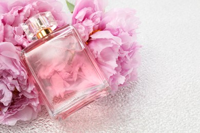 Luxury perfume and floral decor on white plastic surface, space for text