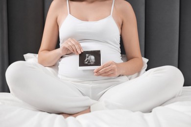 Photo of Pregnant woman with ultrasound picture of baby on bed, closeup
