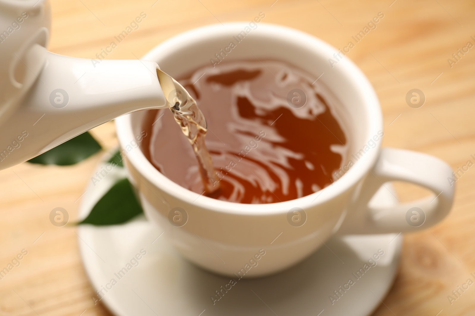 Photo of Pouring tasty tea into cup at table, closeup