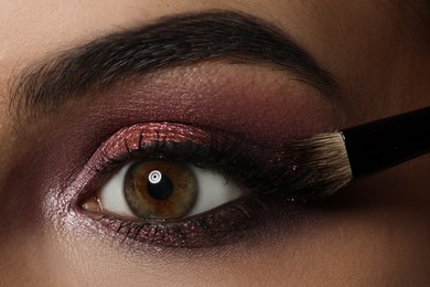 Photo of Applying dark eye shadow with brush onto woman's face, closeup. Beautiful evening makeup