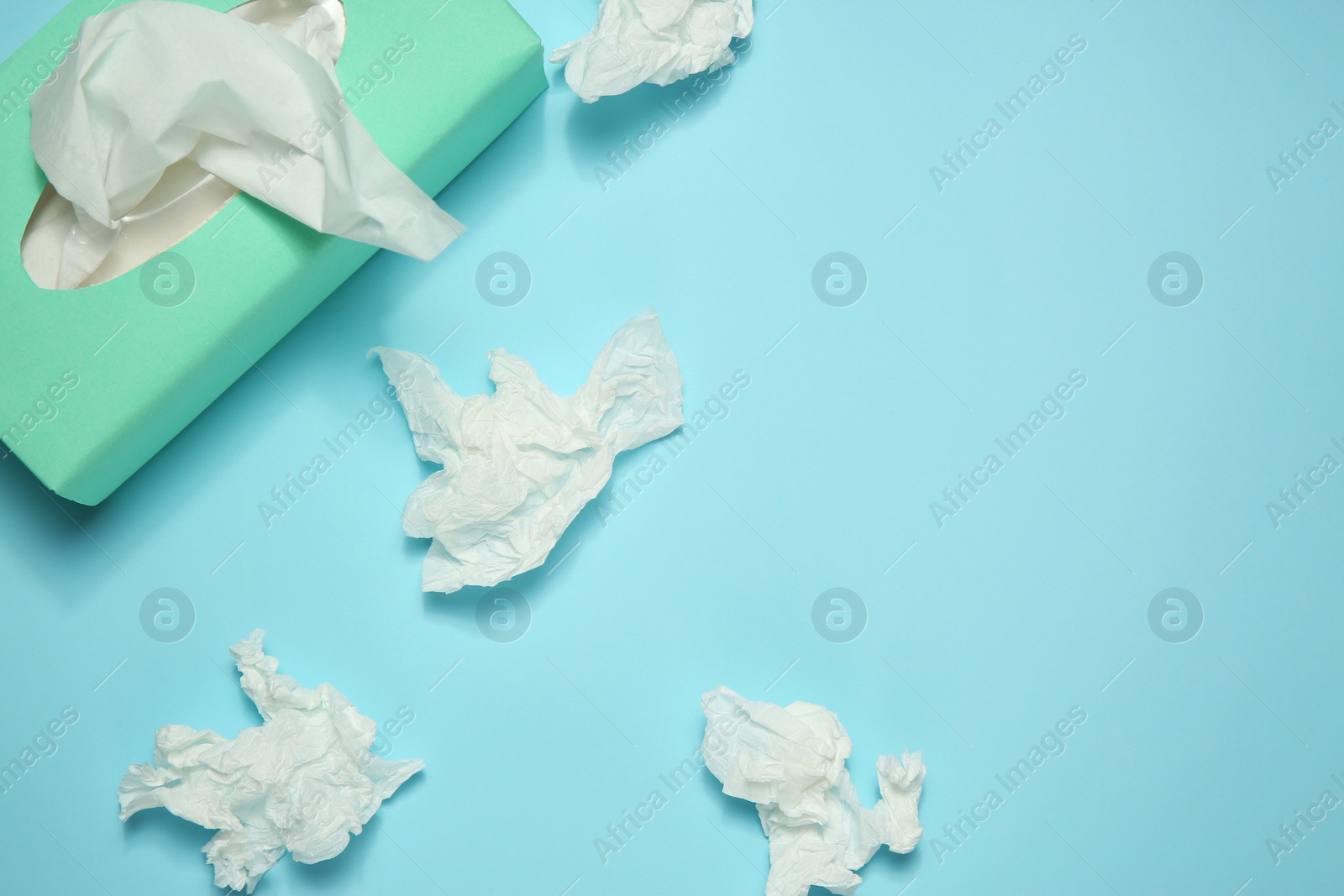 Photo of Used paper tissues and box on light blue background, flat lay. Space for text