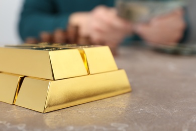 Photo of Stacked gold bars and man counting money at table, closeup. Space for text