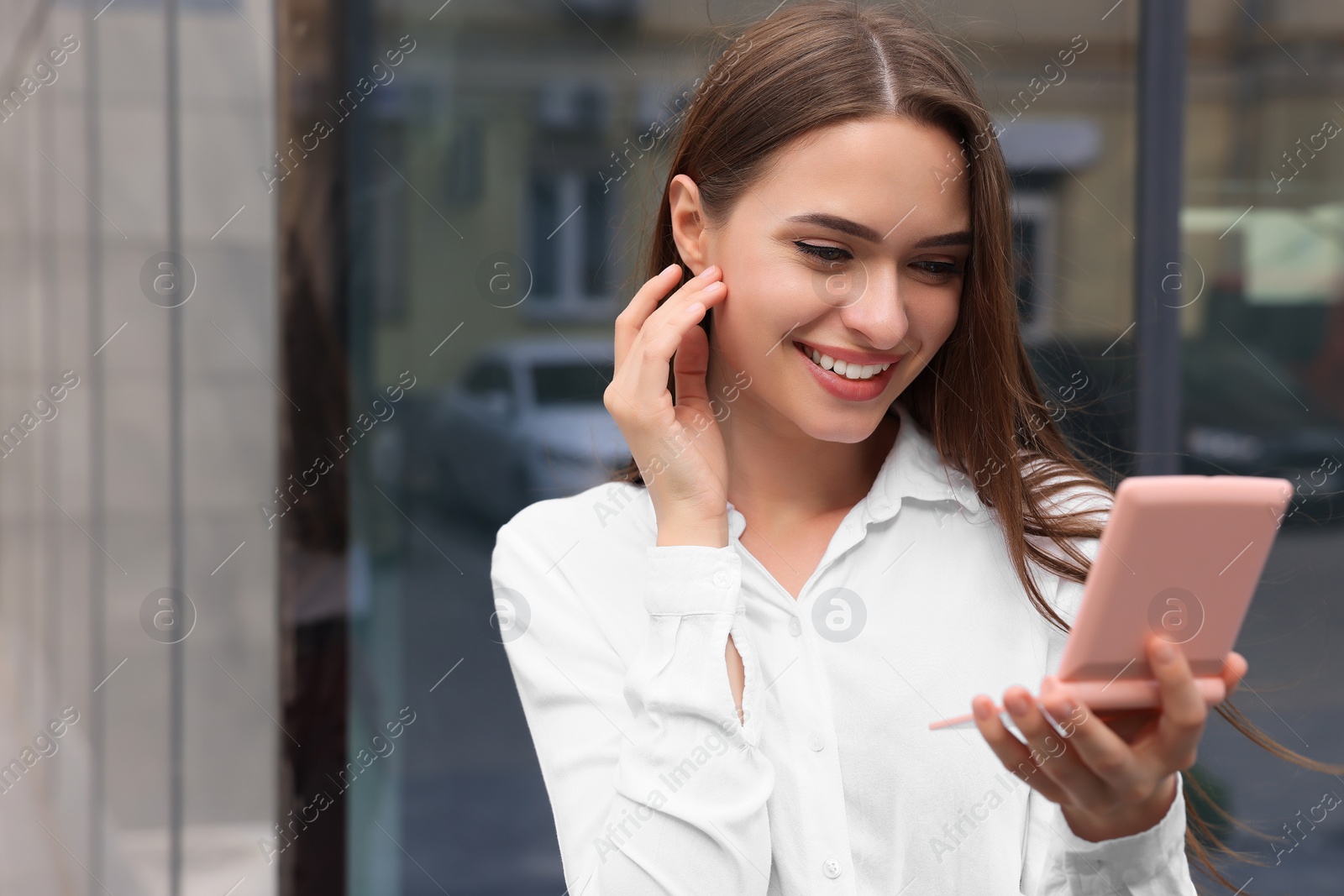 Photo of Young woman looking at herself in cosmetic pocket mirror outdoors, space for text