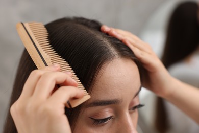 Woman with comb examining her hair and scalp on blurred background, closeup