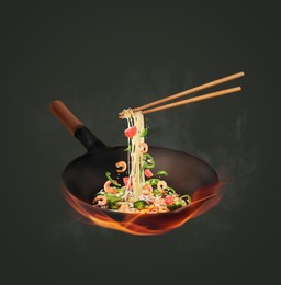 Wok with tasty ingredients and fire on dark background