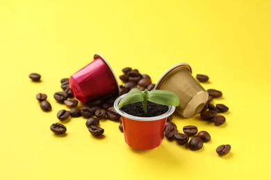 Photo of Coffee capsules with seedling and beans on yellow background