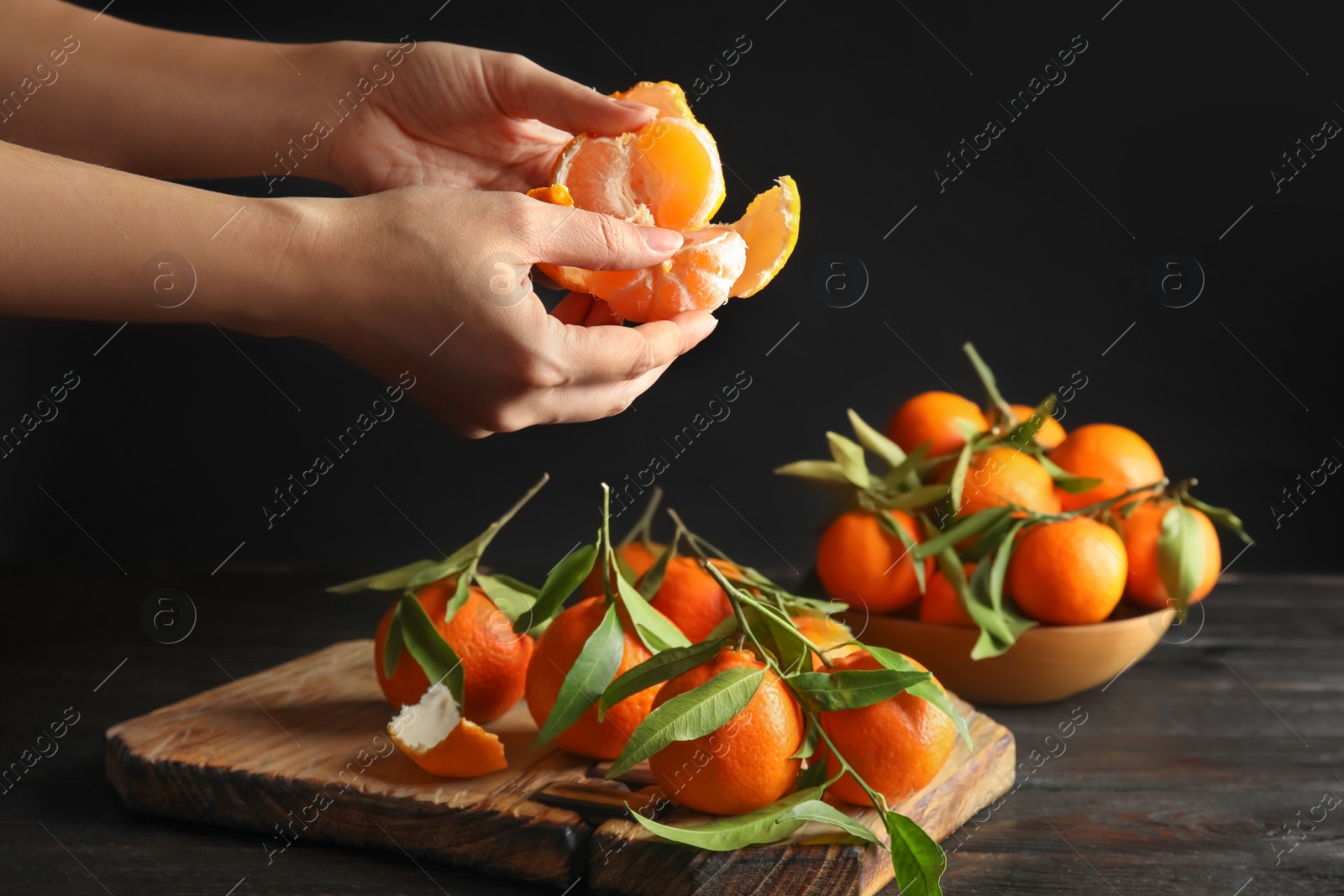 Photo of Woman peeling ripe tangerine over table on dark background, closeup