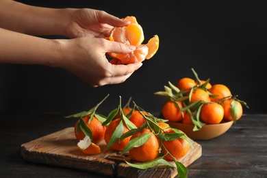 Photo of Woman peeling ripe tangerine over table on dark background, closeup