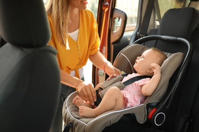 Mother fastening baby to child safety seat inside of car