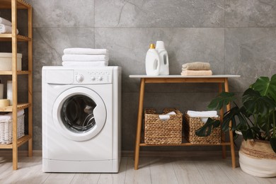 Photo of Storage baskets with towels, detergents, houseplant and washing machine indoors