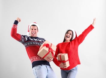 Photo of Beautiful happy couple in Santa hats with Christmas gifts having fun on light background