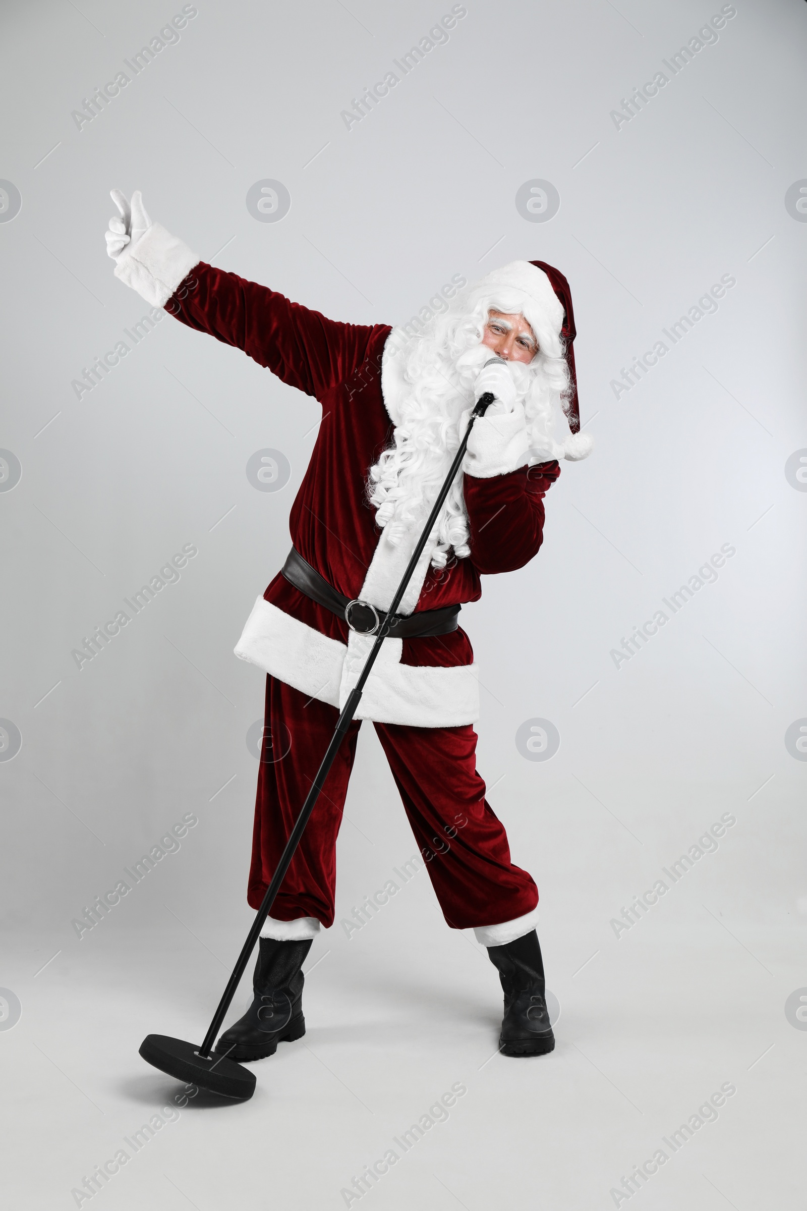 Photo of Santa Claus singing with microphone on light grey background. Christmas music