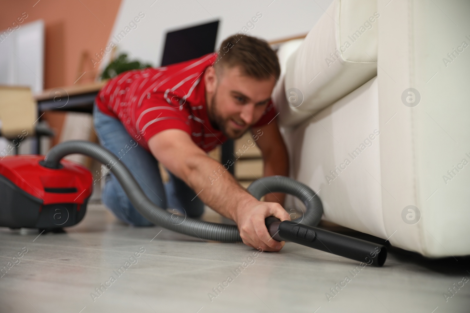 Photo of Young man using vacuum cleaner in living room