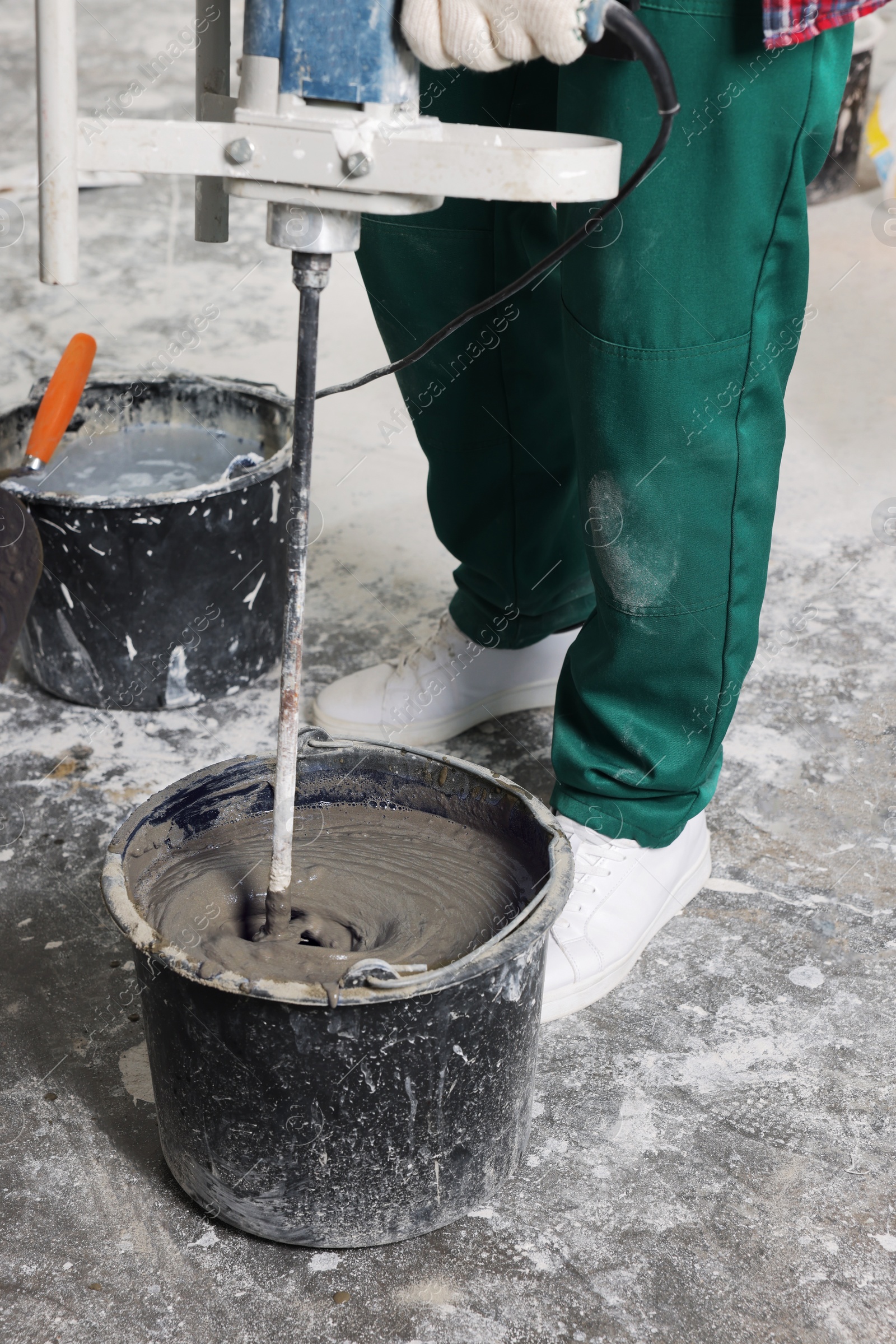 Photo of Worker mixing concrete in bucket indoors, closeup